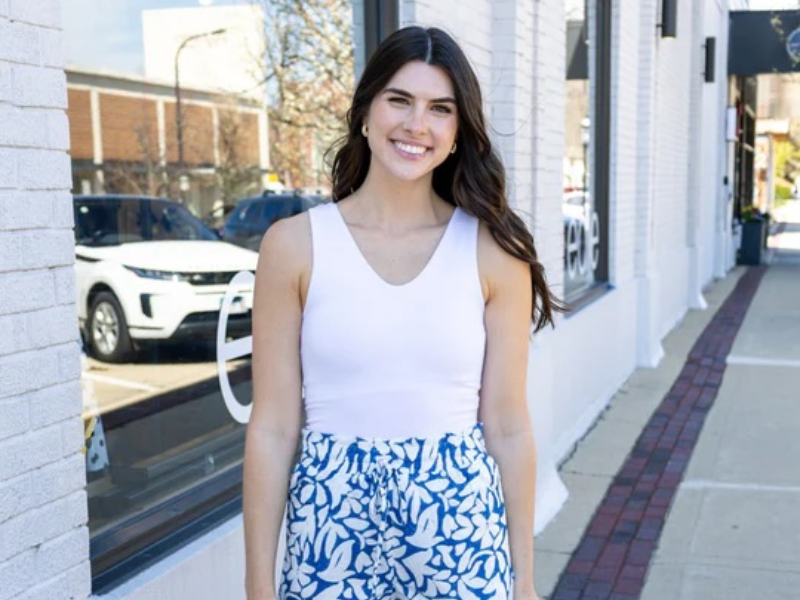 a dark haired woman in a white tank top and blue patterned skirt smiles at the camera